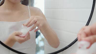 Closeup hand of young woman applying cream or lotion for rejuvenation skin on face while looking mirror in bathroom, woman