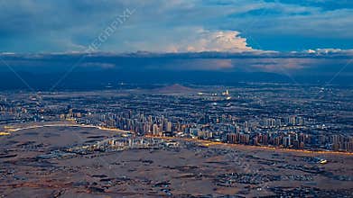 Illuminated city nestled between vast deserts and towering mountain ranges