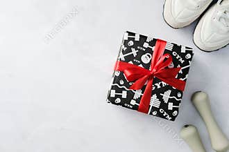 Gym gift box with red ribbon next to sneakers and dumbbells on a marble surface.