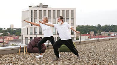 Senior couple practicing yoga outdoors on urban rooftop with city view