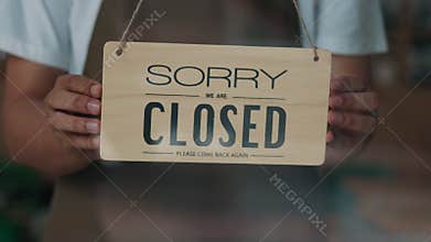Closeup shot of worker hands turning sign Sorry We are closed on cafe door