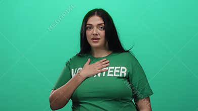Curvy woman volunteer in green shirt stands over isolated green background wall, embodying commitment and community service