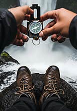 Person holding compass in nature, exploring outdoors, hiking boots and waterfall