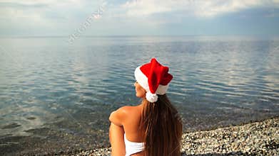 Christmas beach woman: Woman in Santa hat sits, watches ocean, tropical beach, celebrating holidays.
