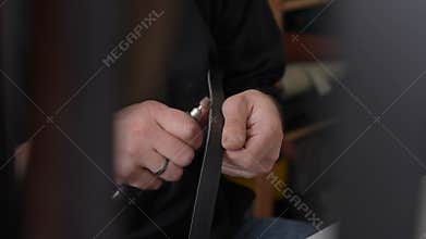 A tanner processes the edges of a leather belt in a workshop. Close-up of woman's hands.