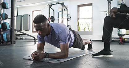 Trainer crouching placing hand on African American male holding plank on mat adjusting posture