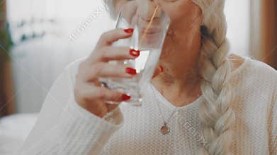 Happy elderly senior woman sitting on bed eating taking vitamins pill holding glass water drinking. Lady pension age