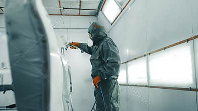 An industrial worker applies paint in a spray booth wearing protective gear