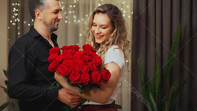 Romantic man gives a gift luxurious bouquet flowers red roses to beloved woman. Happy couple in love on Valentine&#x27;s