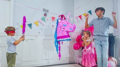Joyful friends swings at a vibrant unicorn pinata on b-day party
