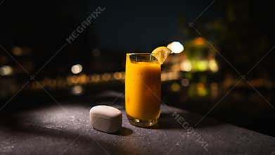 A refreshing glass of orange juice with a lemon slice on a table at night, with soft bokeh lights