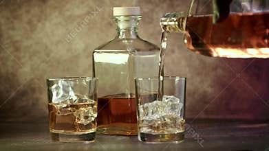 Glasses of whiskey with ice and a bottle of whiskey or brandy on a wooden table.
