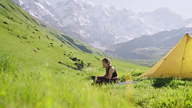 Woman on backpacking trip makes coffee on portable mini gas stove outdoors. She cooks with a pot, then turns off burner