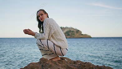 Romantic woman contemplating sea horizon crouching on beach rocks.