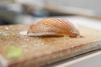 Close-up of a sea bream fry nigiri sushi on a textured cutting board, highlighting the delicate texture and precise knife cuts