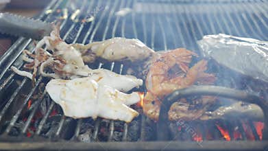 Squid and shrimp roast over glowing embers, turning golden brown as they absorb the smoky heat. The grill crackles with