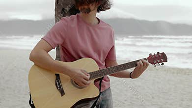 Young musician strumming acoustic guitar by ocean waves on serene beach