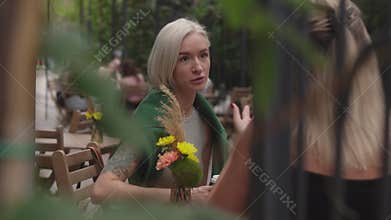 Two Women Friends Chat and Enjoy Coffee at an Outdoor Cafe