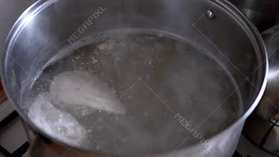 Raw chicken breasts boiling in water inside metal pot for homemade soup
