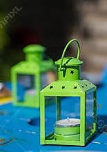 Green lanterns sit on a blue table with candles inside during a sunny day in the garden setting
