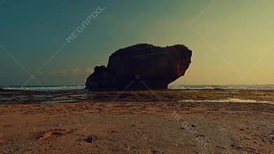 Cinematic ocean waves crashing against a lone rock formation at sunset