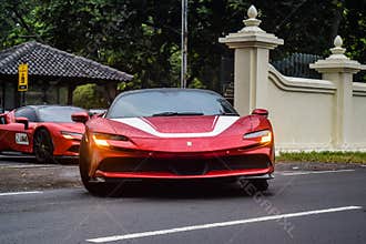 Red Ferrari SF90 stradale Plug-in Hybrid Electric Vehicle PHEV hypercar driving on the wet road after rain