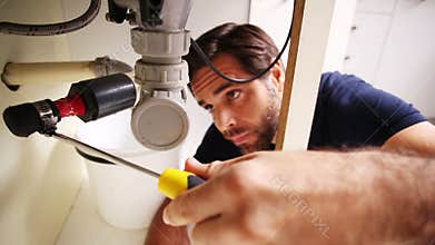 Handsome plumber using screwdriver to fix sink