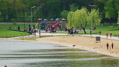 Wide shot of a public park with a playground, families, and a lakeside