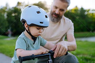 Father helping toddler son learn to ride balance bike for the first time.