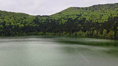 Aerial drone view at low altitude of a calm green lake between foreste