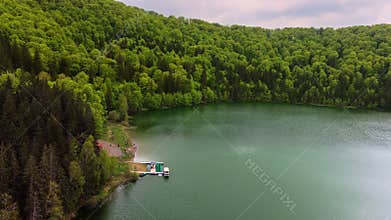 Overhead aerial view of a circular crater lake ringed by forest, Lacul