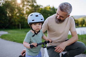Father teaching toddler son to ride balance bike while wearing safety helmet.