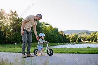 Father teaching toddler son to ride balance bike while wearing safety helmet.