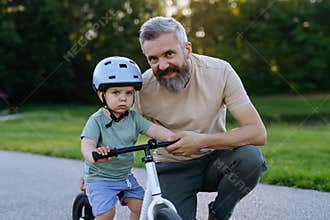 Father helping toddler son learn to ride balance bike for the first time.