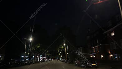 Night urban street with parked cars, streetlights, tall trees, low-rise