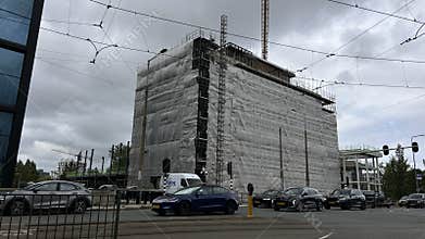 Large wrapped construction building beside busy urban intersection with tram