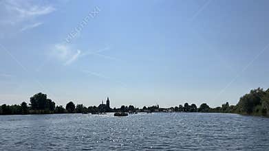 Wide river view with sparkling water, small boats, tree lined banks, and