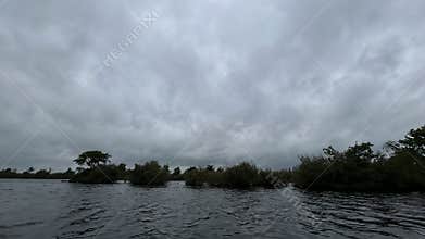 Dark clouded sky over wide water with small tree covered islands, calm
