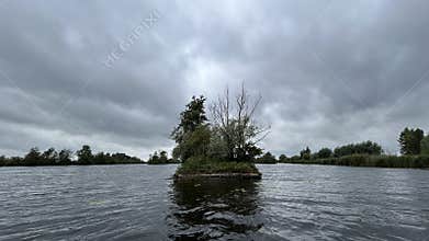 Floating vegetated islet on calm river water beneath dramatic cloudy sky