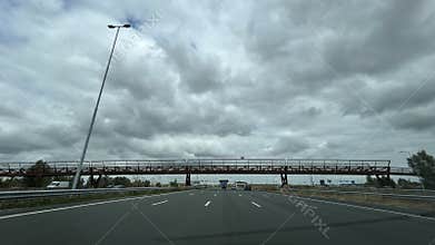 Wide motorway view with heavy cloud cover, long pedestrian bridge crossing lanes