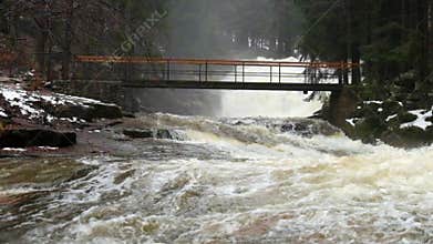 Bridge over troubled water. Huge stream of rushing water masses below small footbridge. Fear of floods.