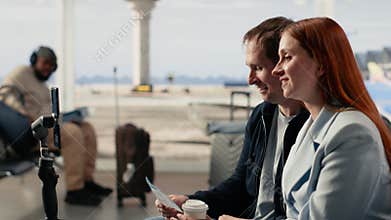 Content creators couple, filming vlog, in airport terminal with tripod