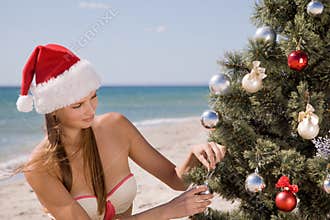 Young woman in Santa hat on beach decorates a Christmas tree balls