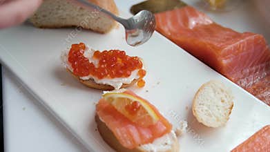 bread with butter and red caviar. red caviar being placed on buttered multigrain bread using a spoon. A can of salmon