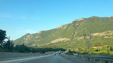 A scenic highway in Turkiye surrounded by mountains and greenery. Road signs indicate speed limits. Clear blue sky enhances the