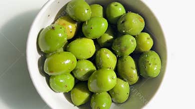 Top down view of marinated whole green olives with herbs and spices in white bowl