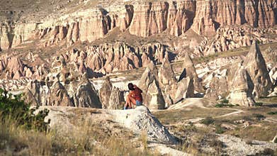 Woman sitting by red sandstone hoodoos in Cappadocia, Turkiye, turkey, travel, valley, fairy chimneys