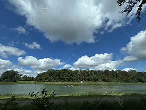 Wide landscape of rowing crew crossing calm lake under dramatic blue sky