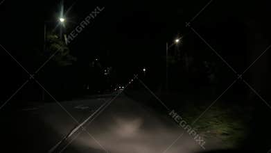 Quiet nighttime road approach toward signalized intersection with glowing