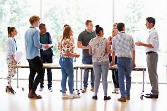 Teacher With College Students Standing By Desks In Classroom